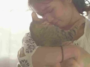 Photo shows a cat owner hugging her cat and looking sad. Example of the emotional impact of having to rehome your pet.